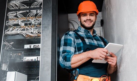 Ein Handwerker steht mit einem Tablet vor einem Schaltschrank