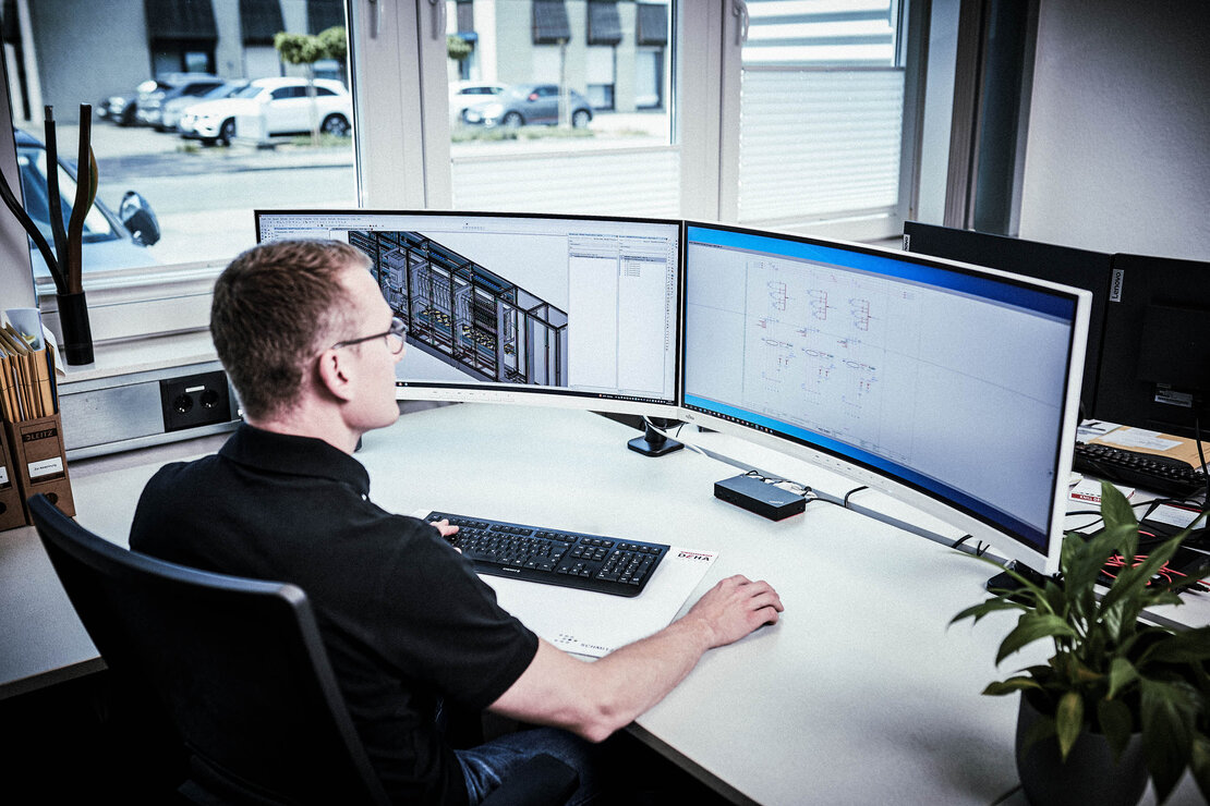 Ein Mitarbeiter sitzt am Schreibtisch vor zwei Bildschirmen.